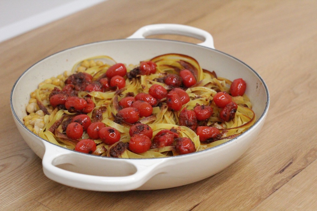 A large shallow cooking dish filled with golden tagliatelle, chickpeas and charred red cherry tomatoes.
